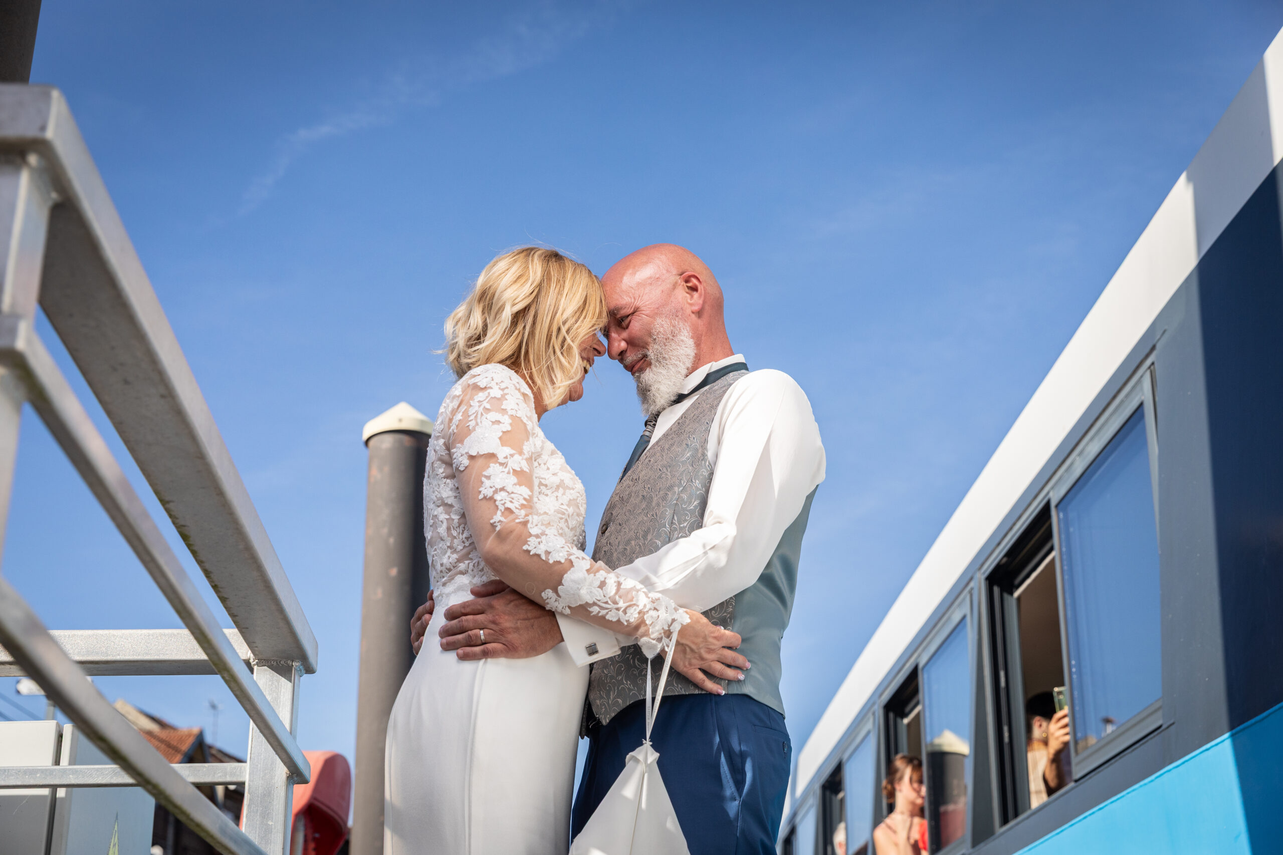des marier qui s'enlace de vent un train sous les regard de passent la femme porte une robe en dentelle et l'homme une chemise blanche et un gilet gris